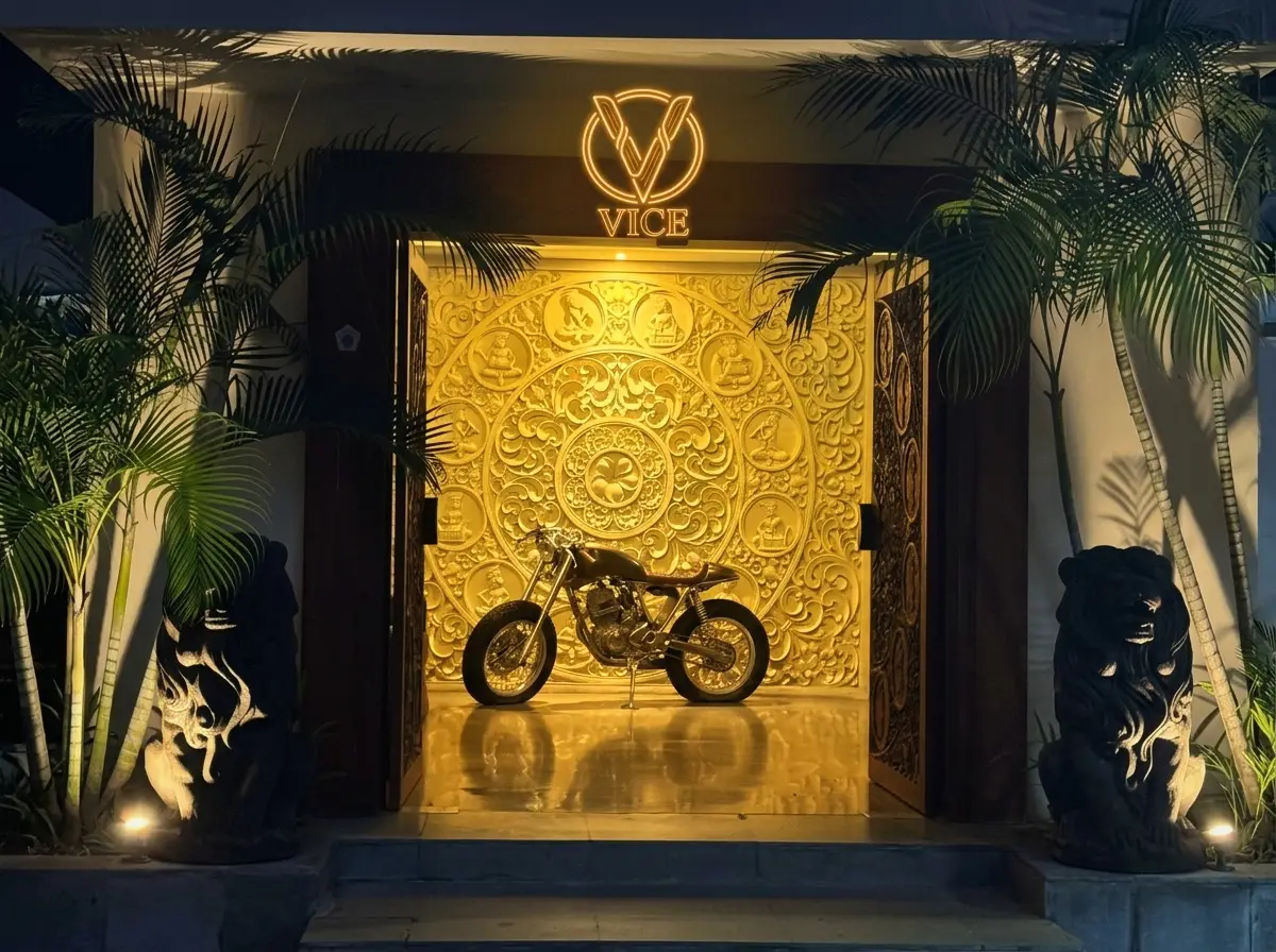 The villa entrance at night: carved gold doors, a motorcycle, and a VICE neon sign above the doorway