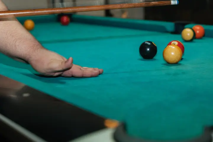 A hand lining up a shot on the pool table