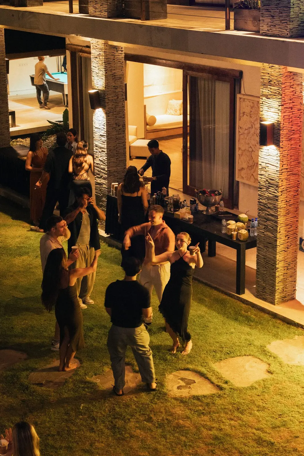 The lawn at night, guests talking in front of the lit villa