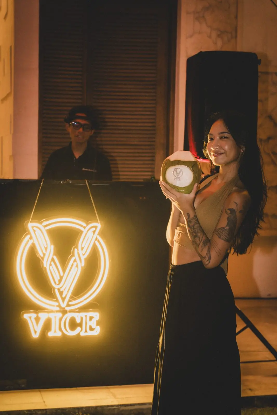 A guest smiling with a coconut by the lit VICE sign